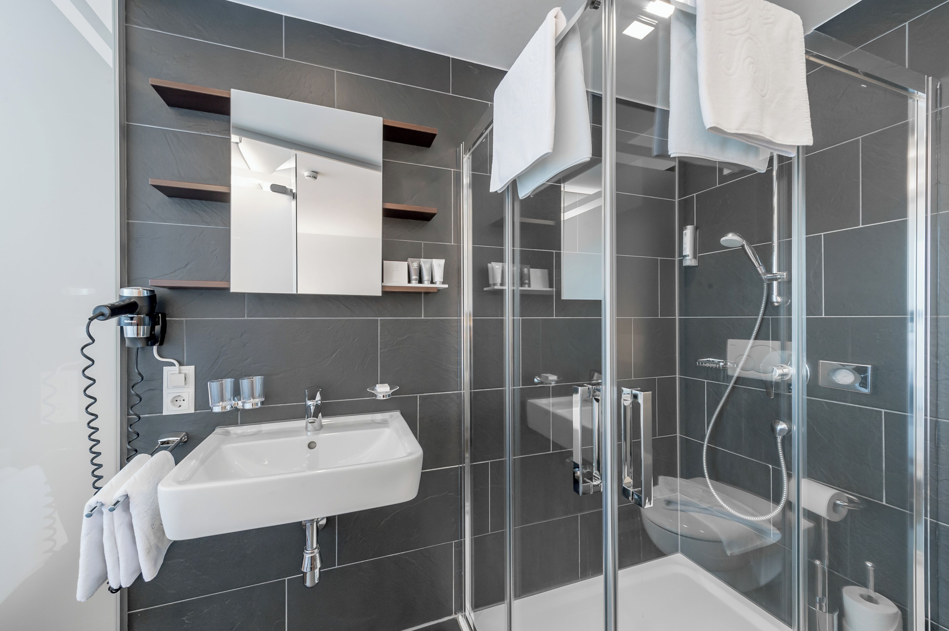 A modern bathroom with a glass-enclosed shower, a white sink, and a mirror above the sink.