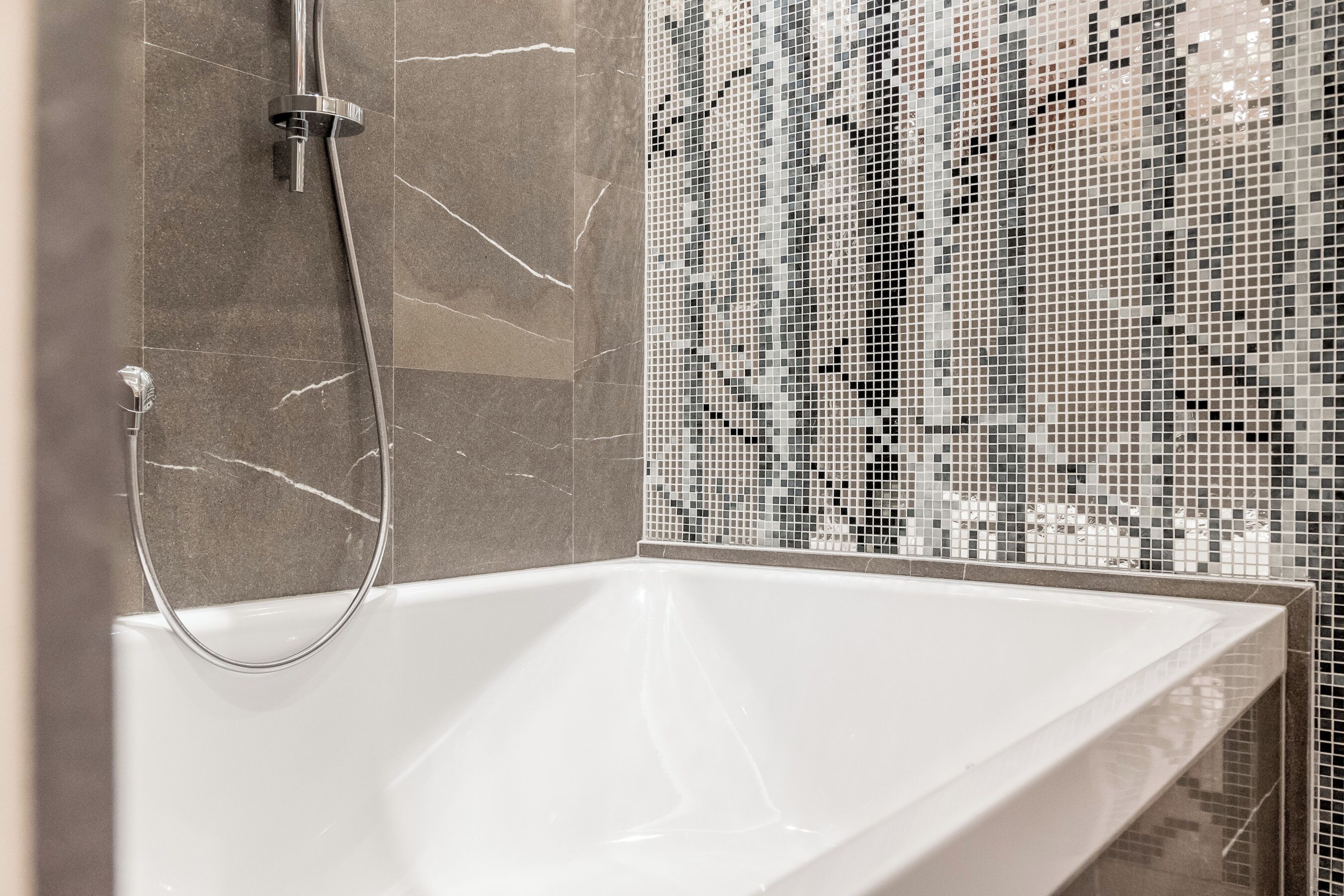 A modern bathroom with a white bathtub, a shower with a chrome faucet, and a mosaic tile wall.