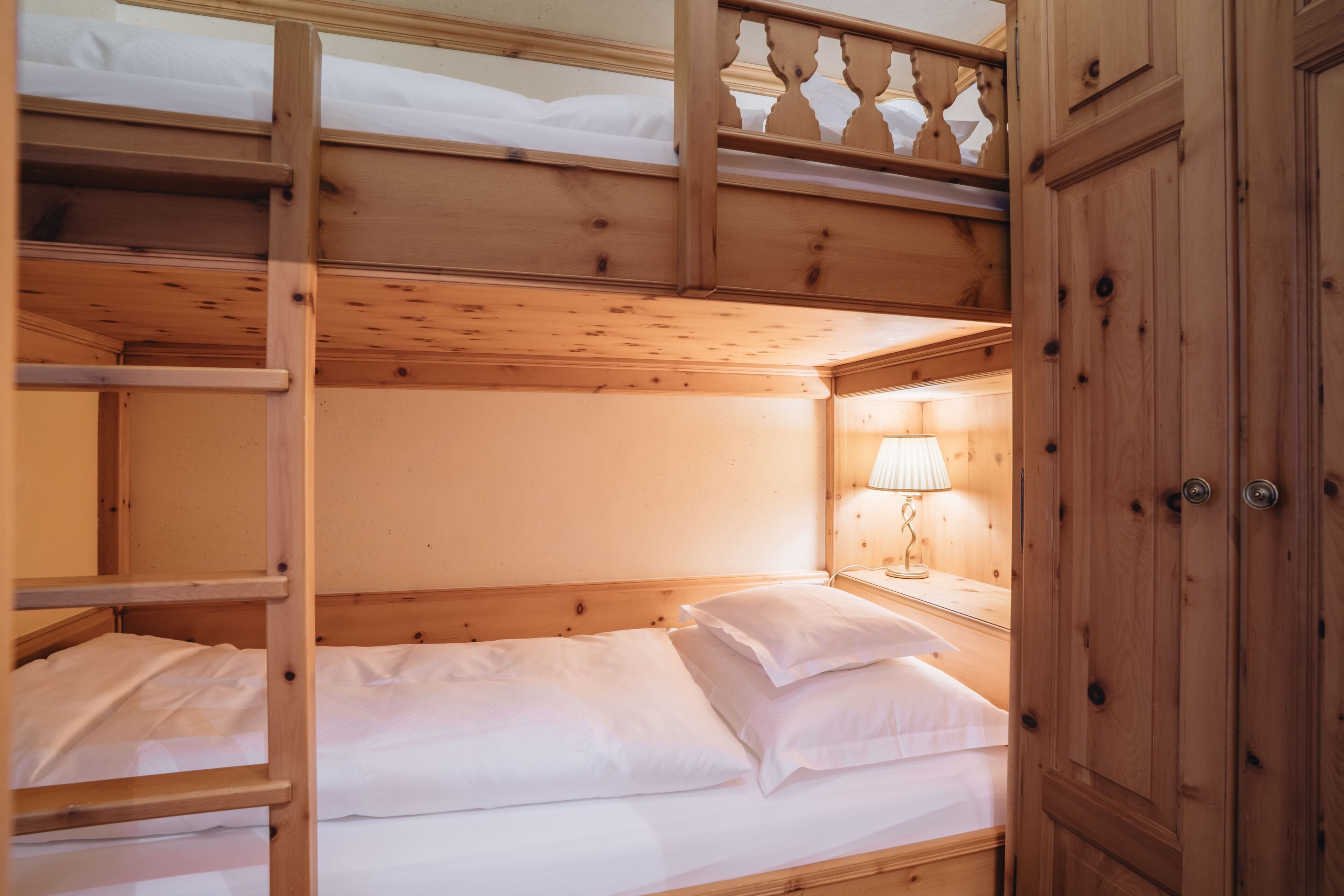 Une chambre avec un lit superposé en bois, une table de chevet et une lampe.
