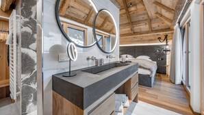 Un baño moderno con un espejo grande, techo de madera y vista al dormitorio.