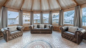 Una habitación con techo de madera, un sofá central y grandes ventanales con vistas nevadas.