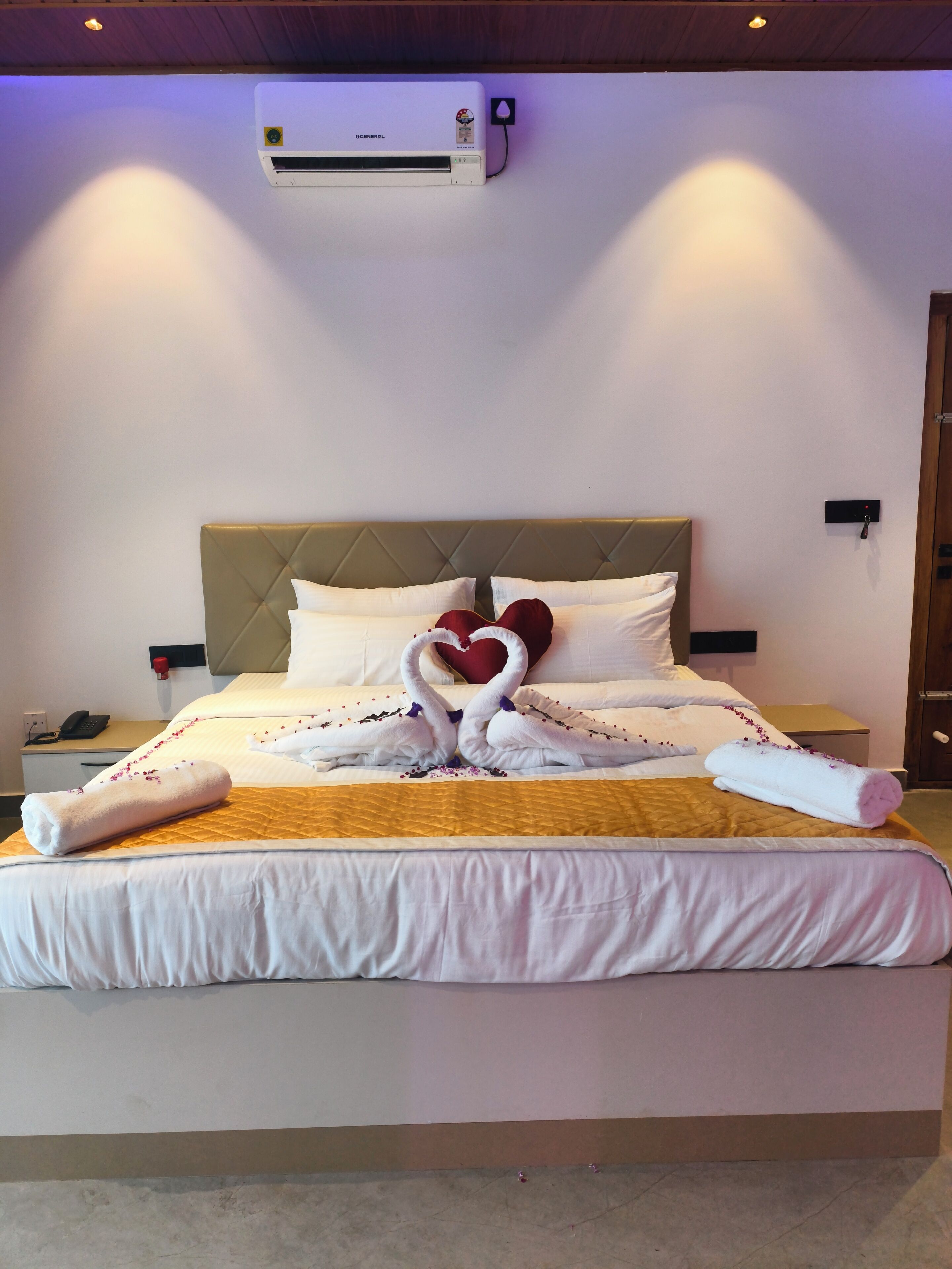A hotel room with a bed, a bedside table, a nightstand, a wall-mounted air conditioner, and a door.