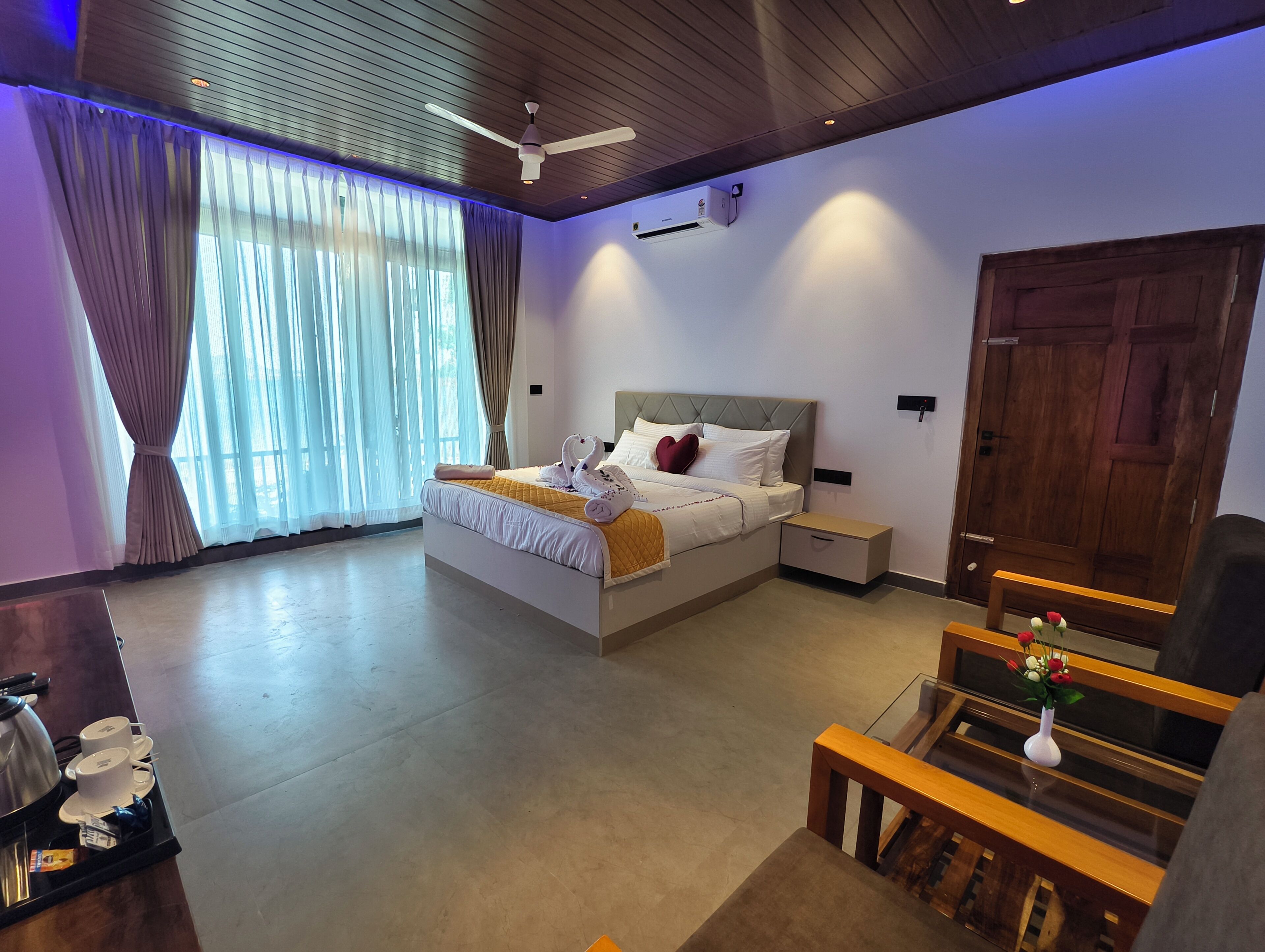 A hotel room with a bed, bedside tables, a desk, a piano, and a large window with curtains.