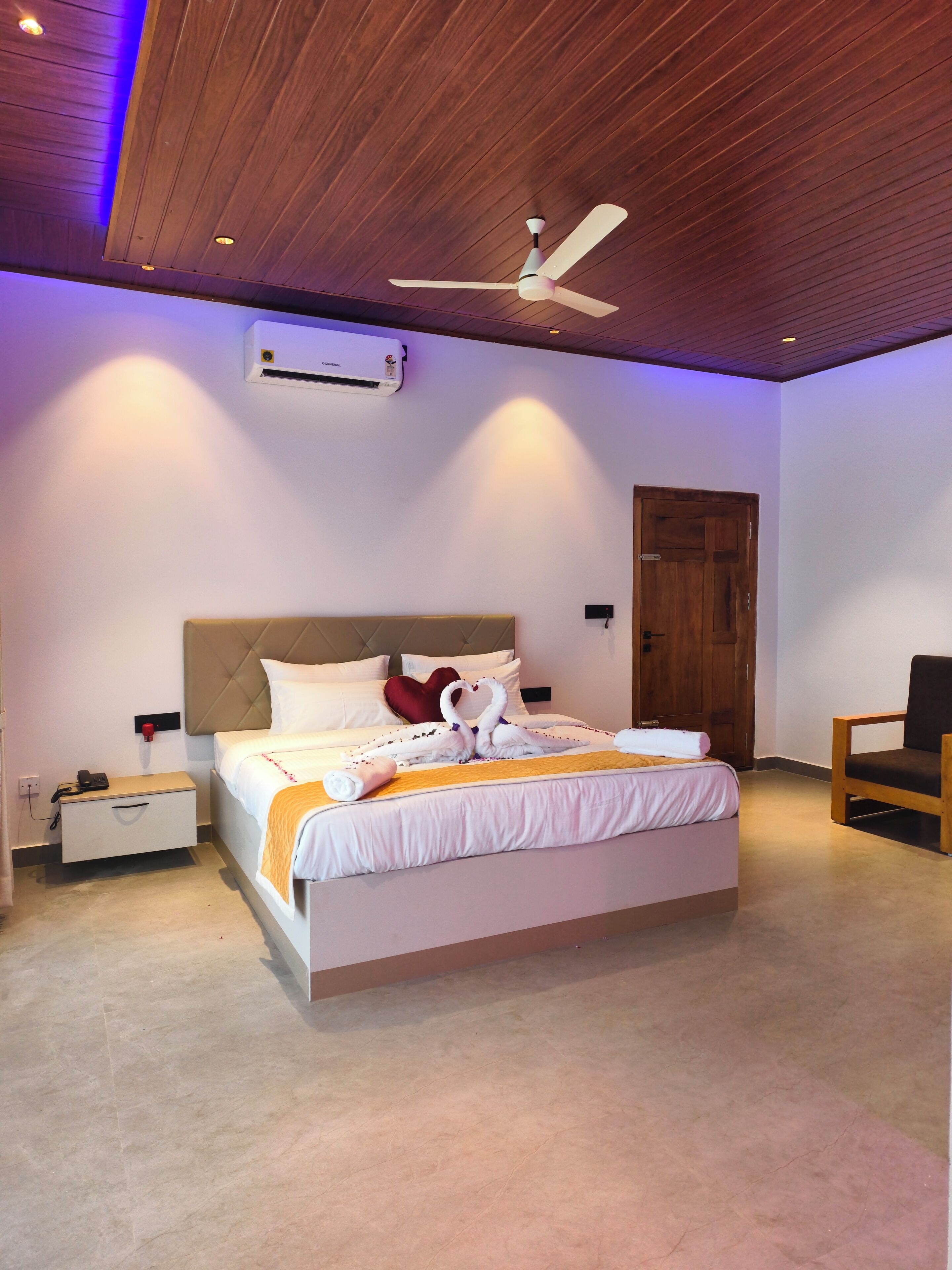 A bedroom with a bed, a bedside table, a chair, a ceiling fan, and an air conditioning unit.