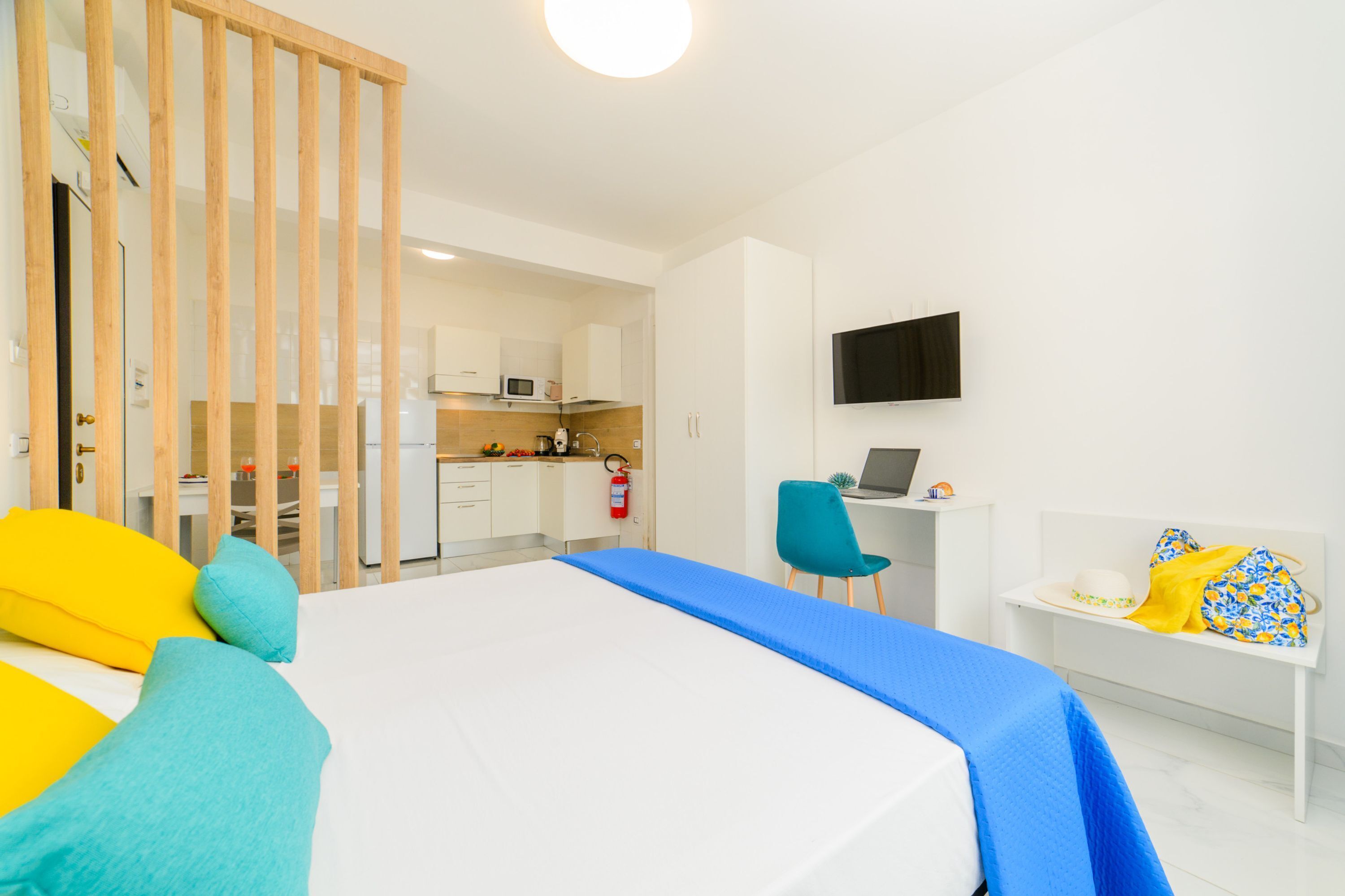 Een hotelkamer met een bed, een bureau met een computer, een stoel, een televisie en een kitchenette op de achtergrond.