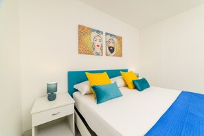 Une chambre à coucher bien rangée, avec un lit, des oreillers, une table de chevet et des œuvres d’art accrochées au mur.