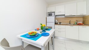 Cocina compacta con armarios blancos, microondas, lavamanos y una mesa de comedor con platos, cuencos y un florero.