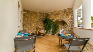 Un patio con dos sillas, una mesa con bebidas, un muro de piedra y una cesta colgante.