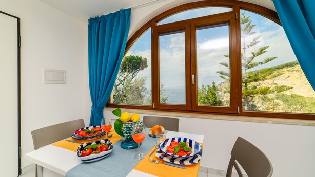 Un comedor con una mesa lista para dos personas, una ventana con cortinas y vistas al exterior.