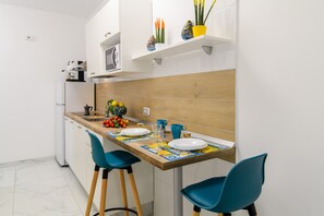 Cocina compacta con cubierta de madera, dos sillas color turquesa y un refrigerador pequeño.