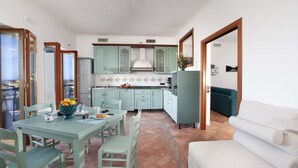 A dining area with a table and chairs, a kitchen with light green cabinets, and a white sofa. - Estate4home - Casa Marelia (Sorrento)