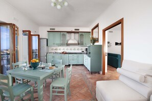 Un coin repas avec une table et des chaises, une cuisine avec des meubles de couleur vert clair et un canapé blanc.