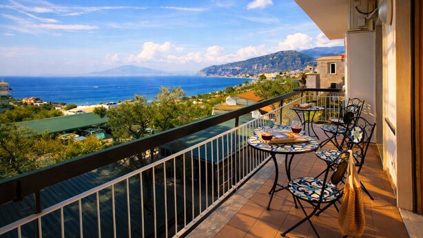 A balcony with a view of the sea, a table with chairs, and a building in the background. - Estate4home - Casa Marelia (Sorrento)