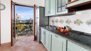 A kitchen with a view to the outside, a dining area with chairs, and a clock on the wall. - Estate4home - Casa Marelia (Sorrento)