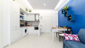 A compact kitchen with a washing machine, a dining table with chairs, and a blue sofa with a floral pillow. - Maison Ann in Sorrento (Sorrento)