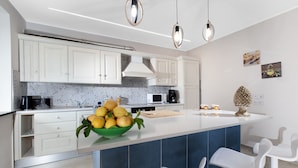 A modern kitchen with white cabinets, a central island with a bowl of fruit, and two bar stools. - Villa Elios in Massa Lubrense (Massa Lubrense)