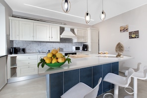 A modern kitchen with white cabinets, a central island with a bowl of fruit, and two bar stools. - Villa Elios in Massa Lubrense (Massa Lubrense)