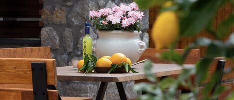 A table with a white vase of pink flowers, lemons, and a bottle of liquor.