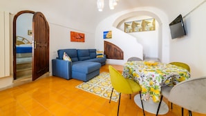 Un espacio habitable compacto con sofá, mesa de comedor, sillas, televisor, obras de arte y una escalera.