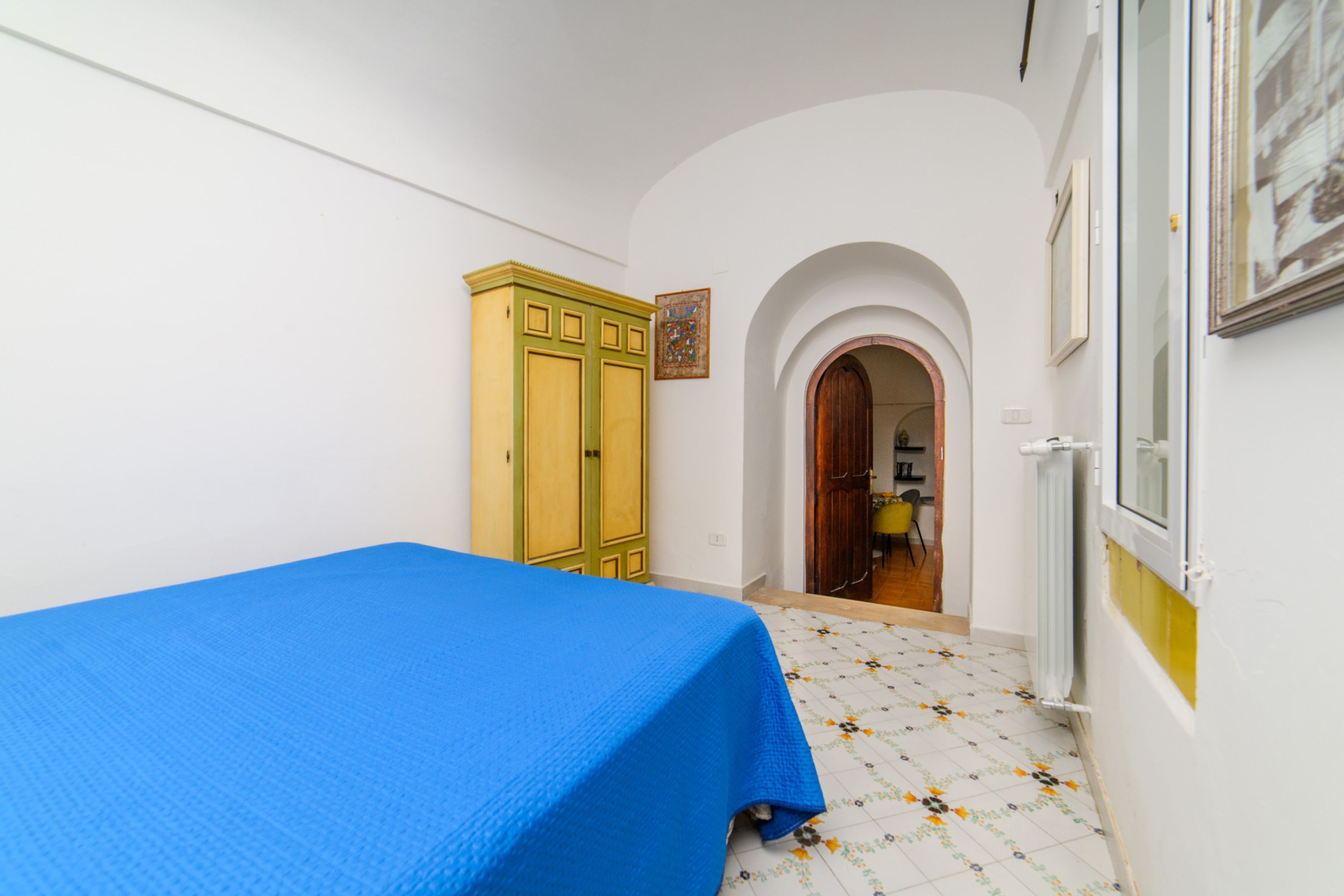 Una habitación con cama, armario, un arco de entrada y un radiador.