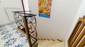 Una escalera con barandilla de metal, piso de baldosas con un diseño azul y un cuadro colorido en la pared.