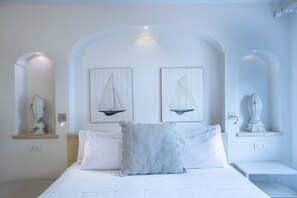 Ein Schlafzimmer mit einem Bett, zwei Kissen, einem Nachttisch, einer Wandskulptur und zwei gerahmten Kunstwerken.