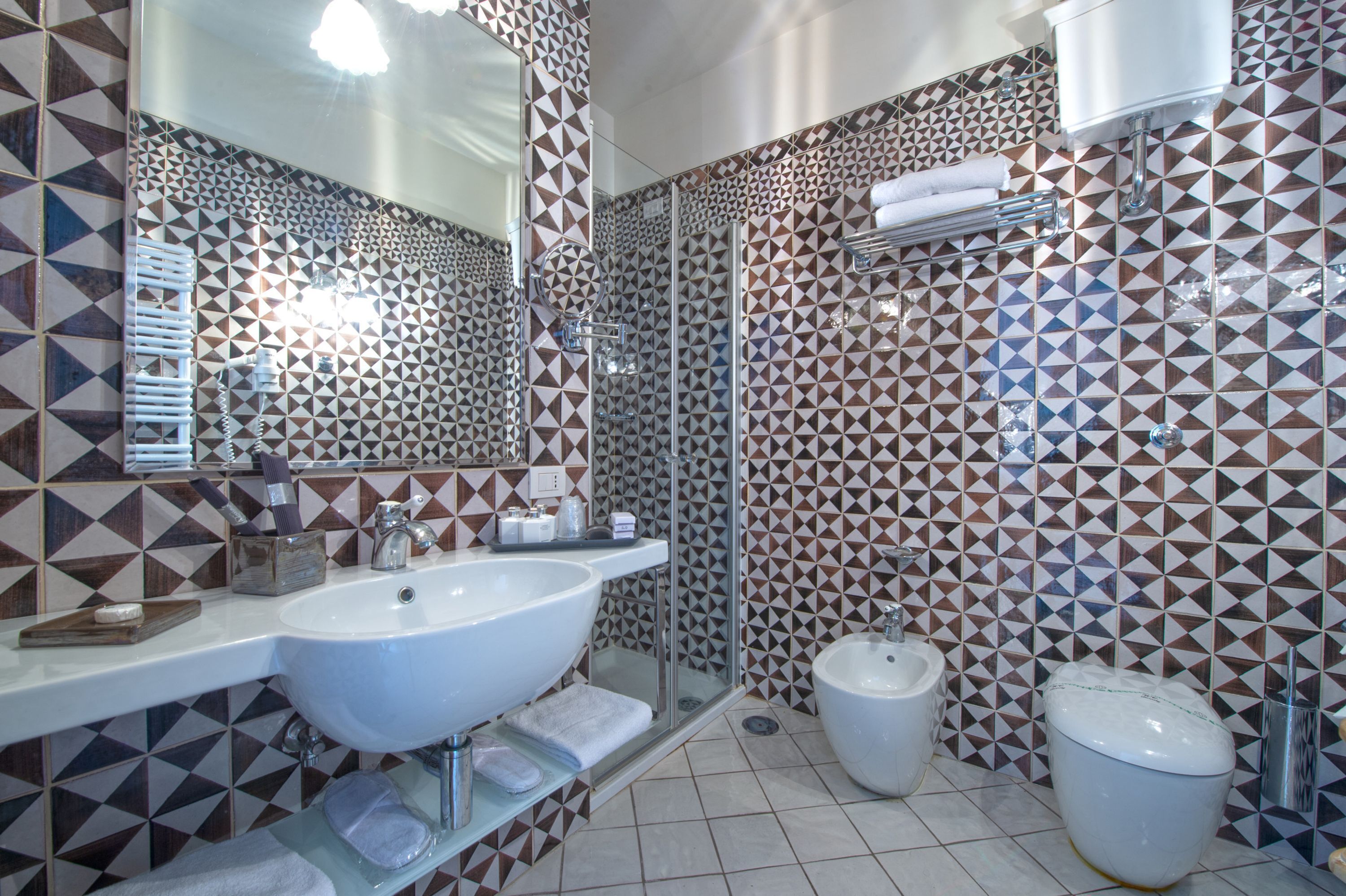 A bathroom with a large sink, mirror, shower, bidet, and tiled walls.