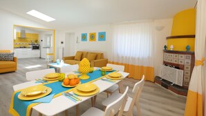 A dining area with a table set for four, a kitchen in the background, and a living area with a sofa and a fireplace. - Relais Villa Chiara in Sorrento (Sorrento)
