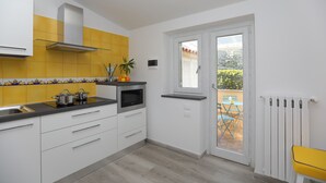 A kitchen with white cabinets, a microwave, and a stove. There is a window with a view of a patio. - Relais Villa Chiara in Sorrento (Sorrento)