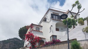 Un edificio bianco con balconi, un muro di sostegno in pietra e montagne sullo sfondo.