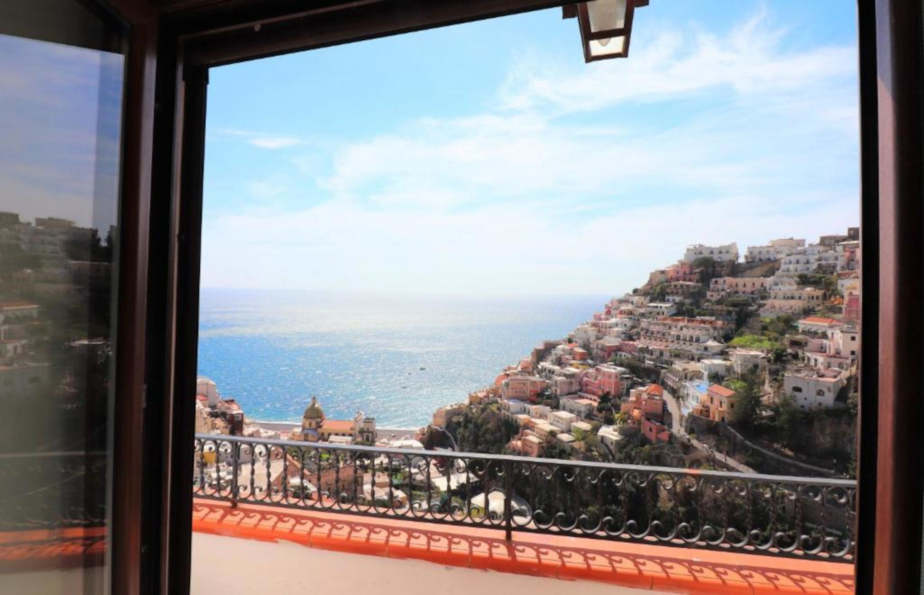 A coastal town with buildings on a hillside, a balcony with a railing, and a clear view of the sea.