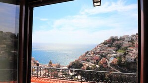 Un borgo costiero con edifici su una collina, un balcone con ringhiera e una vista limpida sul mare.