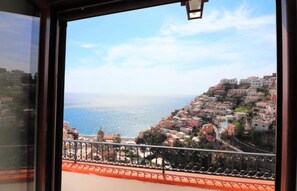 Eine Küstenstadt mit Gebäuden an einem Hügel, einem Balkon mit Geländer und freiem Blick auf das Meer.