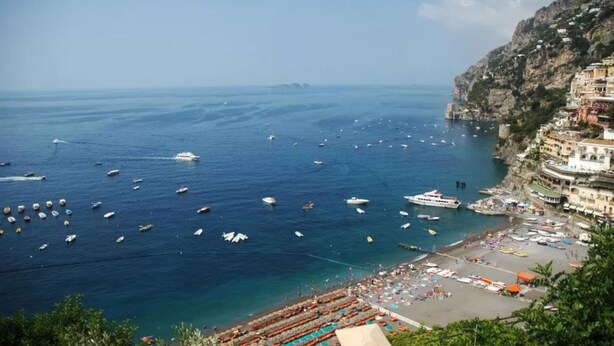 Una località costiera con barche sull'acqua, una spiaggia e edifici a picco sulla scogliera.