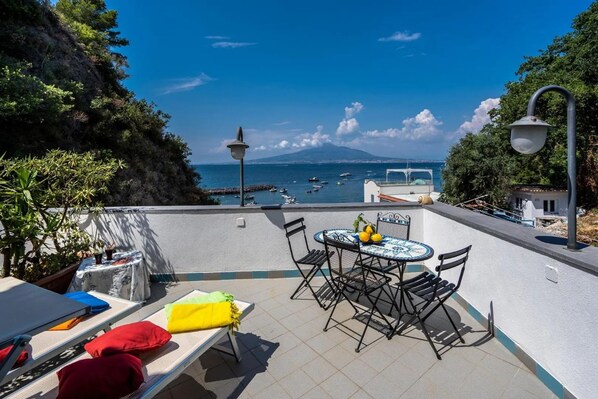 A terrace with a table and chairs, a view of the sea, and a mountain in the background. - Casa Cinzia - Apartment (Vico Equense)