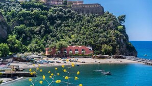 A coastal town with a prominent castle on a hill, a beach with boats, and a building with a red facade. - Casa Cinzia - Apartment (Vico Equense)