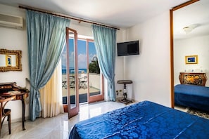 A hotel room with a bed, a desk, a television, and a view of the sea. - Casa Cinzia - Apartment (Vico Equense)