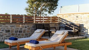 Two wooden lounge chairs with cushions, a stone wall, a wooden fence, and a table with chairs. - Asfendamos Villas - With 2 Private Pools (Mylopotamos)