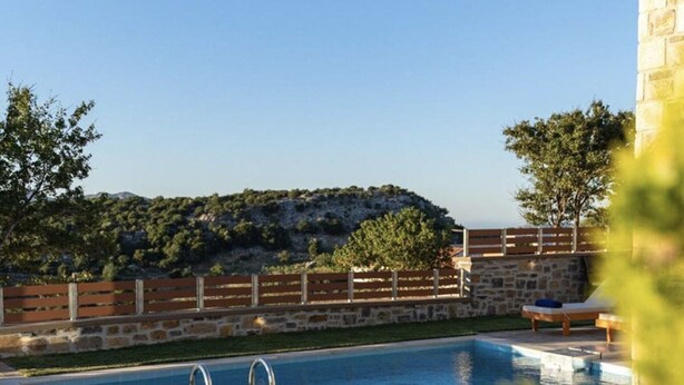 A swimming pool with lounge chairs, a stone wall, and a view of a hill. - Asfendamos Villas - With 2 Private Pools (Mylopotamos)