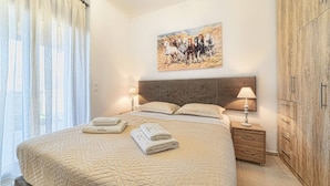 A bedroom with a large bed, two bedside tables with lamps, a wooden headboard, a painting on the wall, and a wardrobe. - Asfendamos Villas - With 2 Private Pools (Mylopotamos)