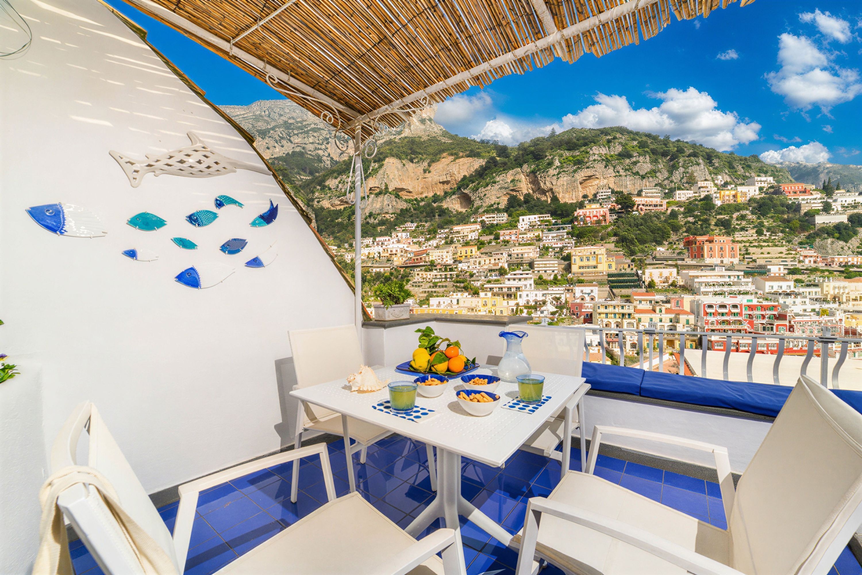 A terrace with a table set for dining, overlooking a coastal town with buildings and cliffs.