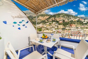 A terrace with a table set for dining, overlooking a coastal town with buildings and cliffs. - Esate4home - Le Vele (Positano)
