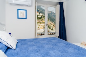 Un dormitorio con cama, ventana con vista a un pueblo en la ladera, y puerta con cortina.