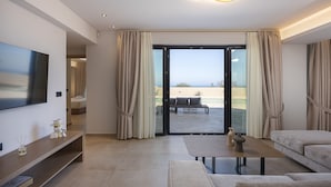 A modern living room with a flat-screen TV, a sofa, a coffee table, and a sliding glass door leading to an outdoor area. - Villa Azure Luxury Sea View Villa (Mylopotamos)
