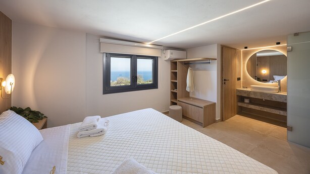 A modern bedroom with a bed, a window, a bathroom with a vanity, and a view of the outdoors. - Villa Azure Luxury Sea View Villa (Mylopotamos)