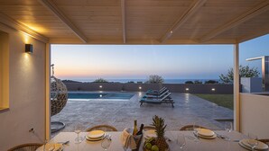 An outdoor dining area with a view of a swimming pool and lounge chairs. - Villa Azure Luxury Sea View Villa (Mylopotamos)