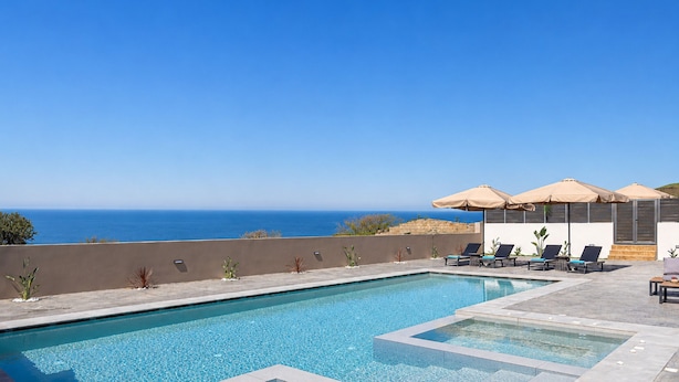 A swimming pool with lounge chairs and umbrellas, overlooking a body of water. - Villa Selene Luxury Sea View Villa (Mylopotamos)