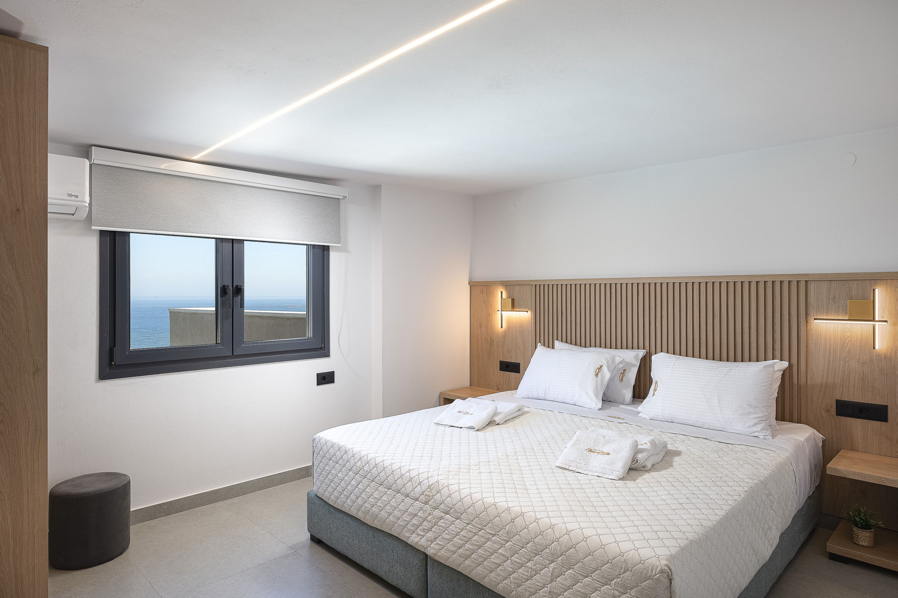 Ein modernes Hotelzimmer mit einem großen Bett, einem Fenster mit Blick, einem Nachttisch und einer wandmontierten Leuchte.