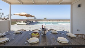 A dining table set for six with a view of the pool and ocean. - Elysioum Pearl Villas - With 2 Private Pools (Mylopotamos)