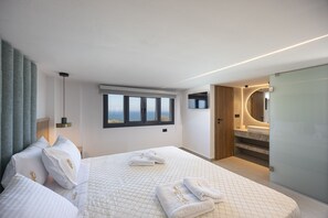Ein modernes Hotelzimmer mit einem großen Bett, Meerblick, einem Badezimmer mit Spiegel und einem Fenster.
